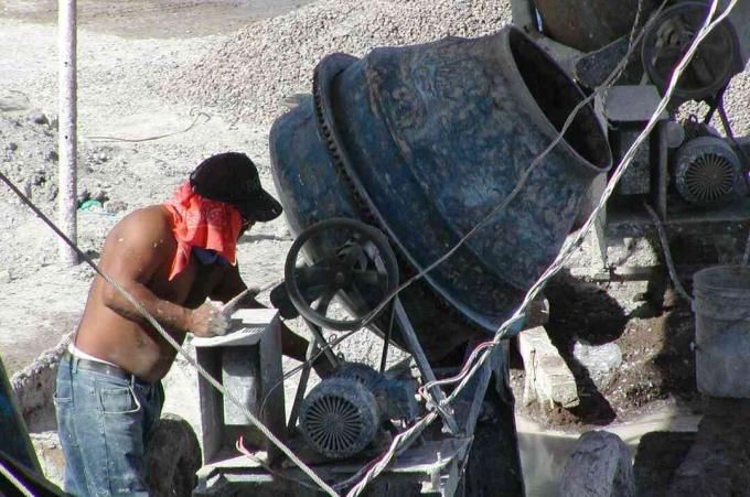 uomo in jeans senza camicia, sciarpa rossa sotto il cappello, lavora una piccola macchina rotonda tipo betoniera