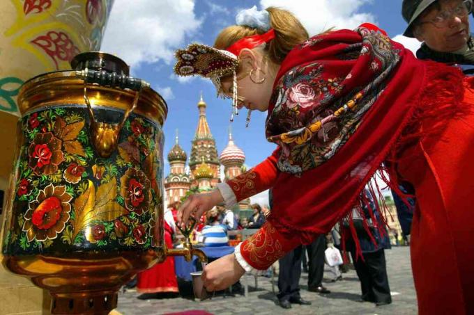 La ragazza russa che indossa vestiti tradizionali versa l'acqua dalla samovar