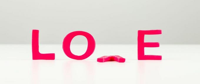 Immagine concettuale con la parola amore in lettere rosse con la V sdraiata a faccia in giù sul tavolo.