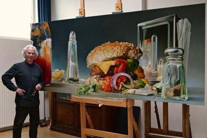 L'uomo sta con l'immagine di grandi dimensioni di un hamburger e sale e pepe shaker.