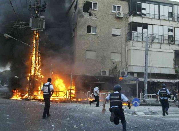 I poliziotti israeliani si precipitano sulla scena di un traliccio elettrico in fiamme e di un edificio danneggiato pochi istanti dopo che una raffica di razzi Hezbollah ha colpito il 13 luglio 2006 nella città settentrionale di Nahariya, in Israele.