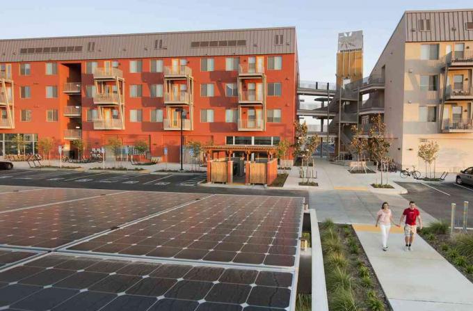 Due persone che camminano vicino a edifici verdi e pannelli solari, in una comunità Zero Net Energy