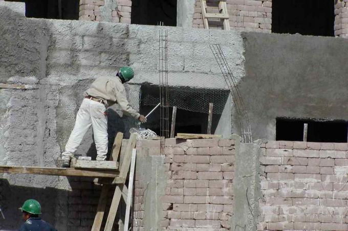 uomo con cappello duro su ponteggi lavorando sul muro di blocchi di terra