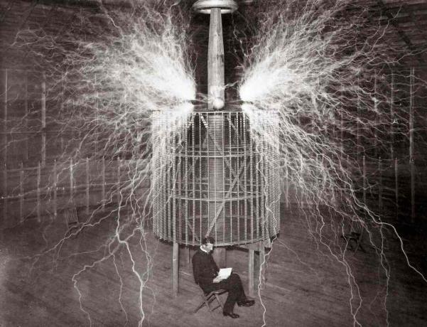 Nikola Tesla seduto nel suo laboratorio di Colorado Springs accanto al suo enorme 
