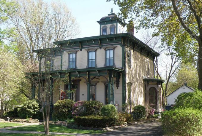 Casa in stile italiano, 2 piani, lato giallastro con finiture verdi e riflessi marrone, una cupola quadrata su un tetto piano, staffe all'interno delle sporgenze del tetto e portico anteriore