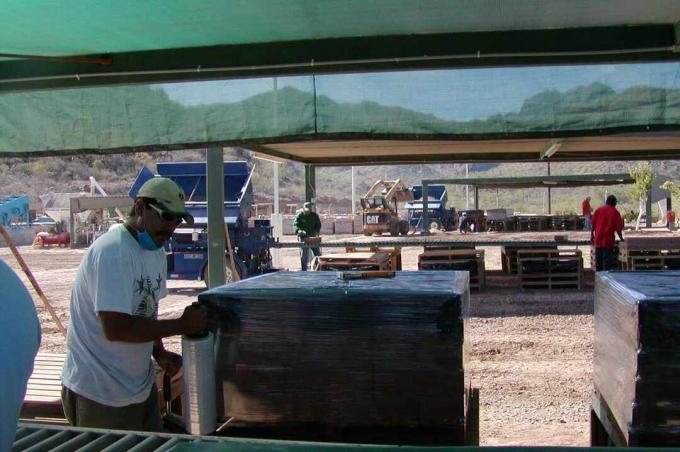 uomo in maglietta bianca che utilizza un involucro di plastica per coprire un pallet di blocchi in una stazione di compressione sotto una copertura simile a una tenda