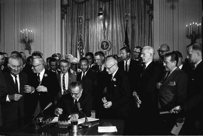 Il presidente Lyndon B. Johnson firma il Civil Rights Act del 1964 mentre Martin Luther King, Jr. e altri stanno a guardare.